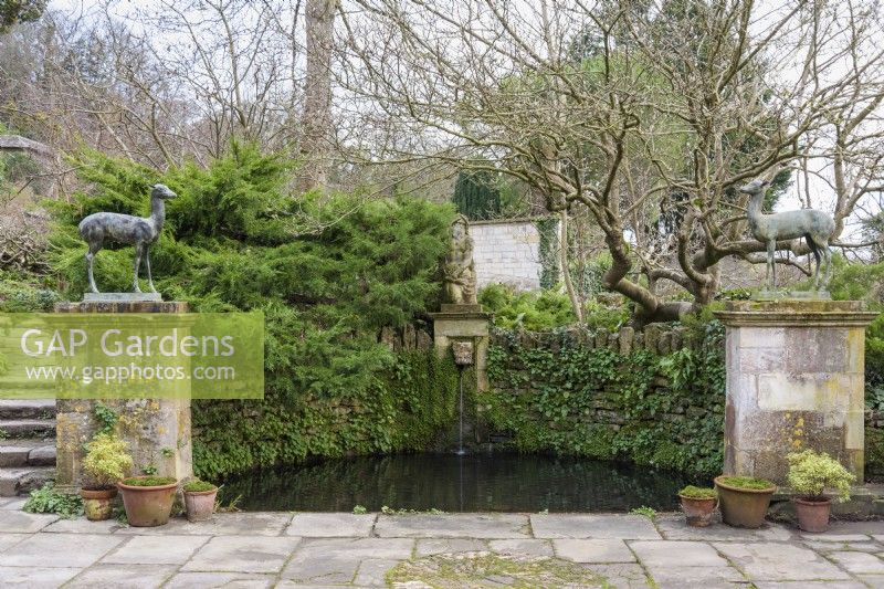 Semi-circular pool with river god and framed by deer on plinths at Iford Manor in January