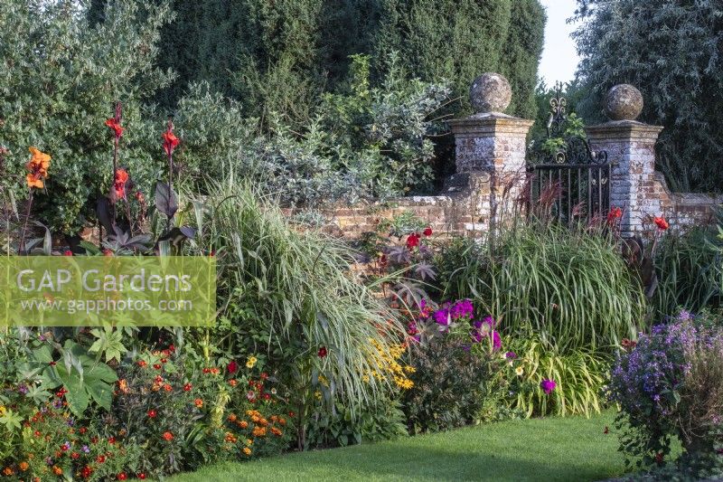 Tropical-style planting sits either side of a wrought iron gate in an old brick wall at The Manor, Little Compton.