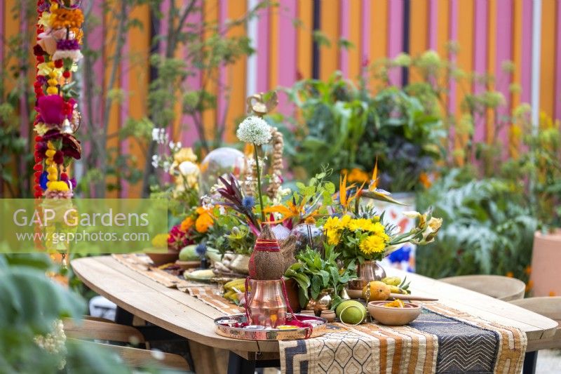 Garden table decorated of Indian ornaments, colourful flowers, fruits and spices in The RHS and Eastern Eye Garden of Unity, designer: Manoj Malde