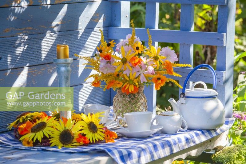 Set for tea and summer flower wreath and bouquet with Rudbeckia, Tropaeolum majus, Solidago and Malva in a glass jar decorated with twine.