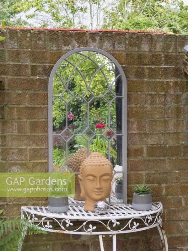 Wrought iron table and mirror against brick wall in cottage garden