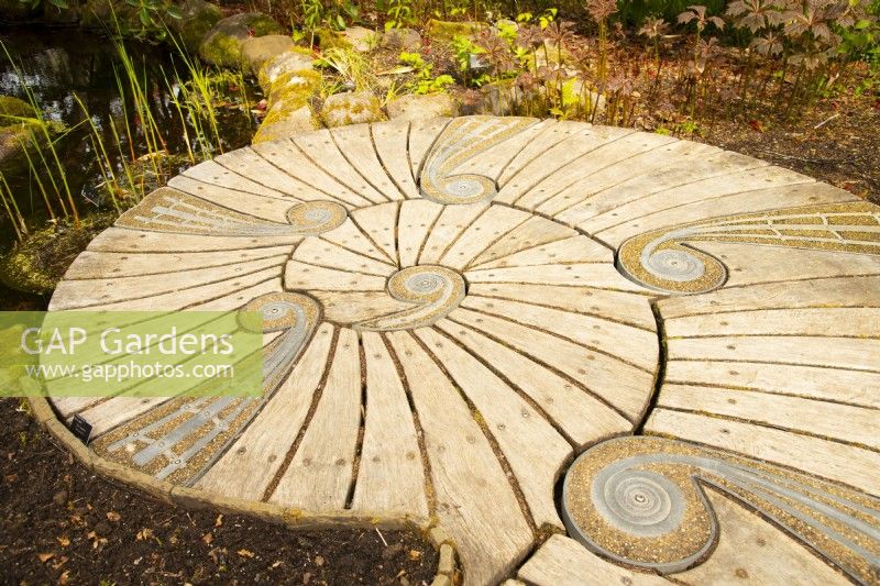 An unusual curved wooden platform with stone and metal inserts next to a small pond in Inverewe Garden.