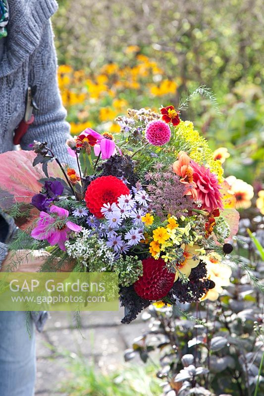 Woman presents self-picked bouquet of flowers in autumn garden 