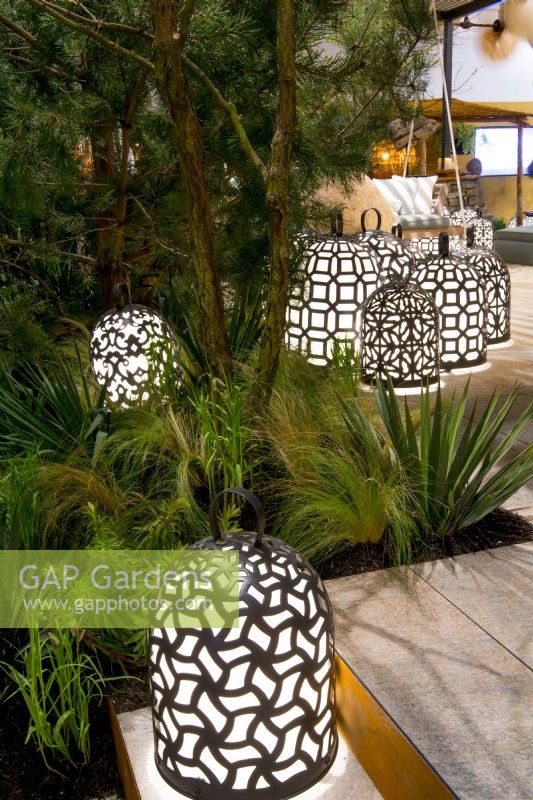 Group of luminescent, handmade brass lamps amongst mixed foliage including Yucca filamentosa, Euphorbia cyparissias ssp wulfenii, Stipa and Pinus sylvestris. Designer: Vetschpartner, Berger Gartenbau and Livingdreams. Giardina-Zurich, Swiss.
