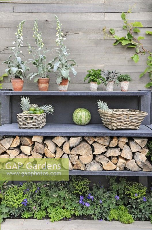 Outdoor kitchen shelves with pots of herbs, Digitalis - foxgloves, Akebia quinata vine, wicker baskets of fruit, logs and small border of shade tolerant plants. 

The Big Green Egg garden

Design: Nicola Harding 

RHS Chelsea Flower Show 2013