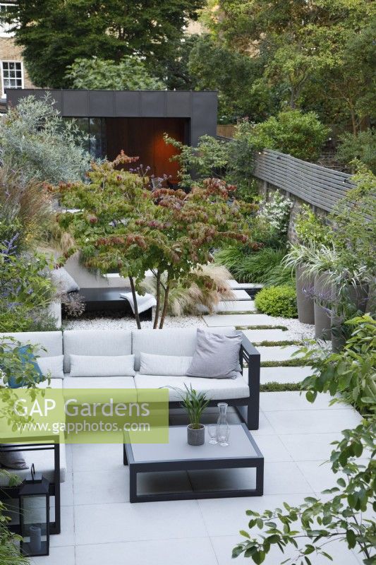 Overview of this city garden with the sitting area with multistem Parrotia persica, sun lounger and path leading to the zinc clad bulding 