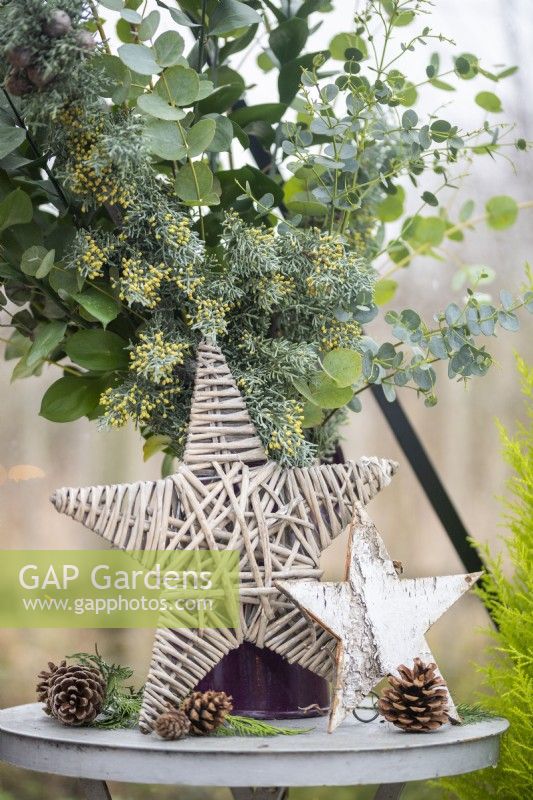 Wicker and birch stars on table with pinecones and a jug of sprigs