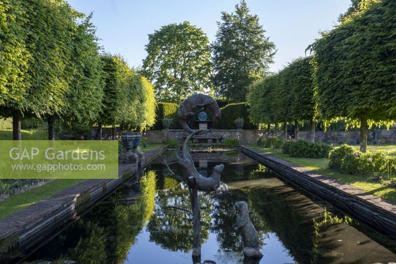 Ornamental sculptures of otters by Susie Wilson frolic above a formal pond which mirrors the surrounding formal garden.