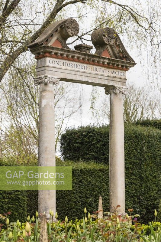 The Triumphal Arch with lettering in Latin. Yew hedges. April. Spring.