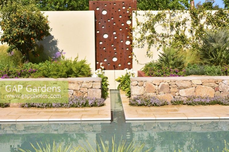 Wall with steel panel with feature a water cascade, flowing into a rill that runs to the main pool and stones raised beds with exotic plants in Mediterranean garden. June
Designer: Alan Rudden


