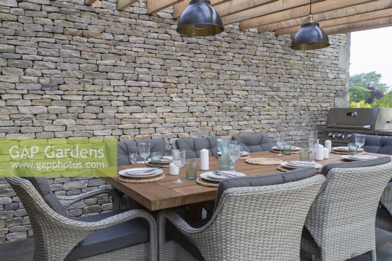 Outdoor dining area under a wooden pergola with Cotswold stone boundary wall - 'The Cotswold Garden' - designer Mark Draper Graduate Gardeners - RHS Malvern Spring Festival 2024