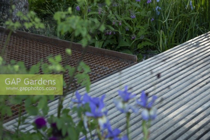 Water permeable grid steel and slatted oak decks, junction detail, with flood resillient planting. The WaterAid Garden at RHS Chelsea Flower Show 2024. Gold Medal. Designers: Tom Massey and Je Ahn.