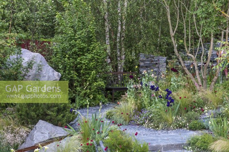 A scree style garden built from slate and boulders is planted with irises, perennials and grasses.