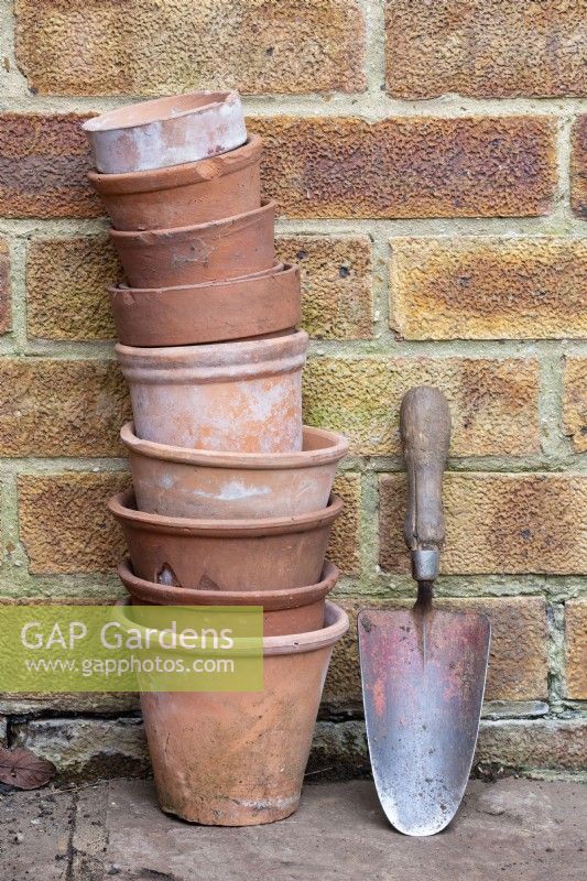 Terracotta pots and trowel against a brick wall