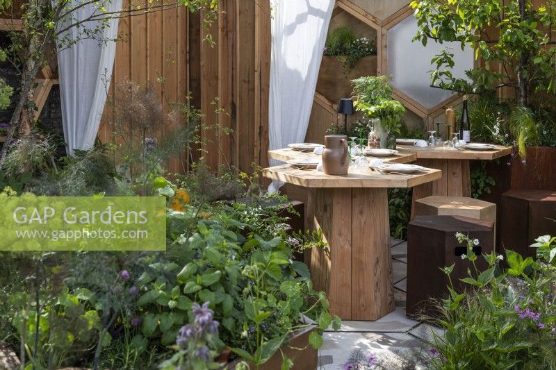 Dining area in small garden with modular hexagonal-shaped furniture made of wood and rusted steel. View through herbs grown in a container. Designer: Louise Checa, Bord Bia Bloom 2024