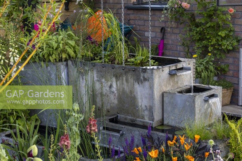 Salvaged galvanised containers are used as a water-gathering system - 'Flood Re: The Flood Resilient Garden' - designers Naomi Slade and Ed Barsley - RHS Chelsea Flower Show 2024
