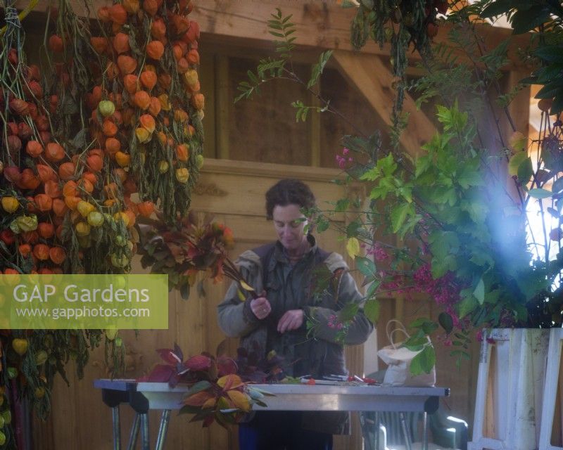 Interior barn workshop where seen here reflected in a mirror, specialist foliage florist, Zanna Hoskins works with Autumn fruits and leaves gathered from her garden for use in seasonal arrangements. November, Autumn, Dorset, UK.