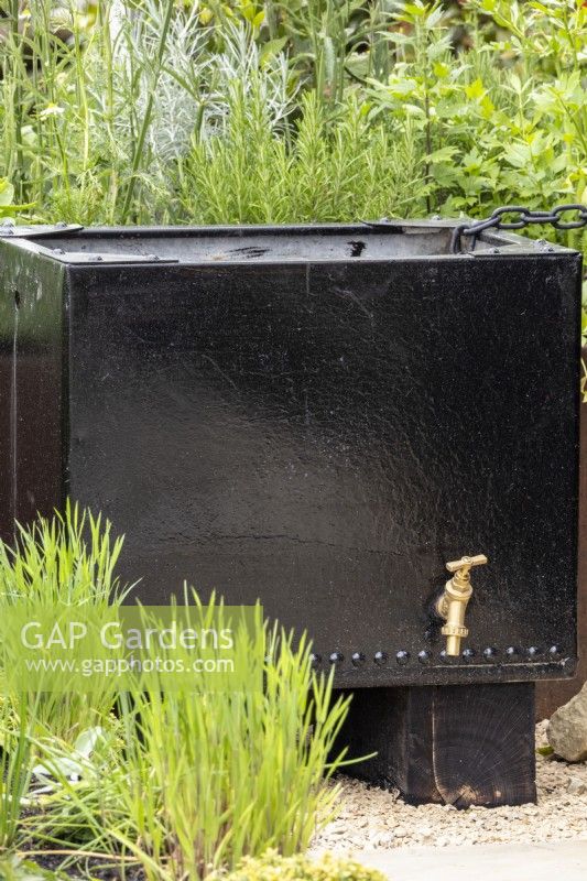 A reclaimed black metal container is used for water collection and storage