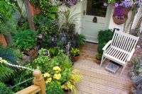 Chair on deck in small town garden, packed with plants in pots, Bristol