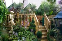 Small town garden in Bristol packed with plants in pots. Raised decking, steps and statue of Pan