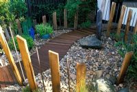 'Zen Seashore Garden' - Small, low maintenance pebble garden with stone boulders, winding wooden path, and wooden and metal post fence.
