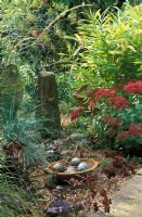 Gravel garden with garden ornaments - stone obelisk and terracotta dish with ceramic eggs in September