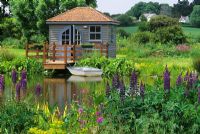 Boathouse by pond with Lupinus - Lupins flowering in foreground