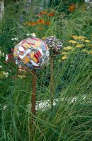 Decorative mulit-coloured mosaic balls on stakes surrounded by grasses - Crisis Garden, Hampton Court Flower Show 2005  