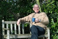 Mr Richard Ayres (retired Head Gardener from Anglesey Abbey, National Trust) sitting on wooden bench in Richard Ayres' Garden, Lode, Cambridgeshire