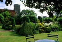 Table and chair on lawn with border of Buxus pyramids, Taxus fastigiata and perennials -  Church in background - Saling Hall, Essex