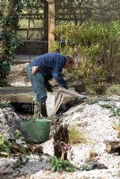 Man maintaining the bed of a garden stream, repairing the sides 