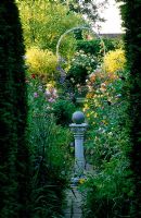 Vista through the circle to a white arch with Rosa and Aquilegias - Woodchippings, Northants 