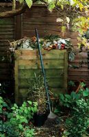 Compost bin made from recycled wooden pallets in back garden with metal rake in Autumn  