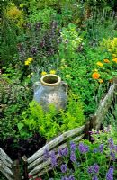 Miniature hurdles made from split ash define the edge af a herb garden that has an old oil Mediterranean oil jar as the centrepiece