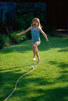 Young girl playing with a hosepipe in the garden