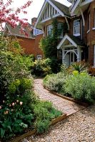 Front garden with curved path with  Tulipa 'Douglas Bader' and Euphorbias