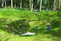 Child running around grass earth sculpture in spring woodland 