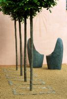 Two rounded metal seats in front of pink walls with sundial and row of clipped Carpinus trees in foreground - Lladro's Sensuality Garden, Chelsea 2003 