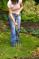 Girl using a garden fork to aerate a lawn in autumn