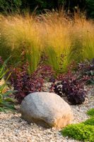 Gravel border with a rock, Stipa tenuissima, Salvia and Sedums in Richard Jacksons garden.