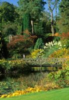 Bridge across pond with Cortaderia selloana in sloping garden - Cholmondeley Castle,  Chesire