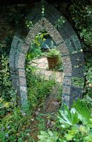 Mosaic mirror with shells, pebbles and tiles is surrounded by Hedera 'Goldheart', Polemonium caeruleum and Fatsia japonica