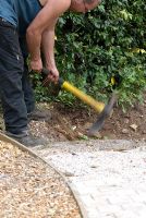 A pick axe being used to break up the soil and remove rubble to make a flower border