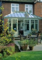 Conservatory at rear of house. Patio with table and chairs and Rosa 'Canary Bird'