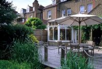 Sub-tropical urban garden. Seaside style fencing around decked seating area with umbrella - Drybrugh Road London