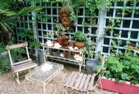 Seats in shady gravel area beside metal and glass etagere and table - antique terracotta mask mounted on trellis