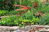 Ornamental kitchen garden with a chicken sculpture made from recycled machinery parts and retaining walls of salvaged concrete slabs and roof tiles