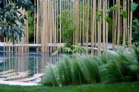 Pool with bamboo poles and raied walkway. Grasses in foreground. Garden in the Silver Moonlight, Design Haruko Seki and Makoto Saito. Sponsor - Royal Palm Residences Seychelles, Urban Regenerate Association of Niigata Supported by - The Great Britain Sasakawa Foundation, The Japan Society
