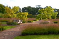 Drifts of grasses including Molinia caerulea ssp. Caerulea and seating area within The Walled Garden at Scampston Hall designed by Piet Oudolf