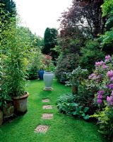 Mixed herbaceous border of mature trees and shrubs with stepping stones in lawn, leading to ceramic container used as focal point - Courtwood House, Staffordshire NGS